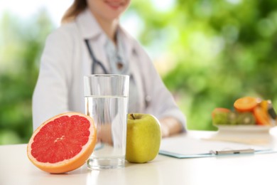 Glass of water, fresh fruits and blurred view of nutritionist outdoors