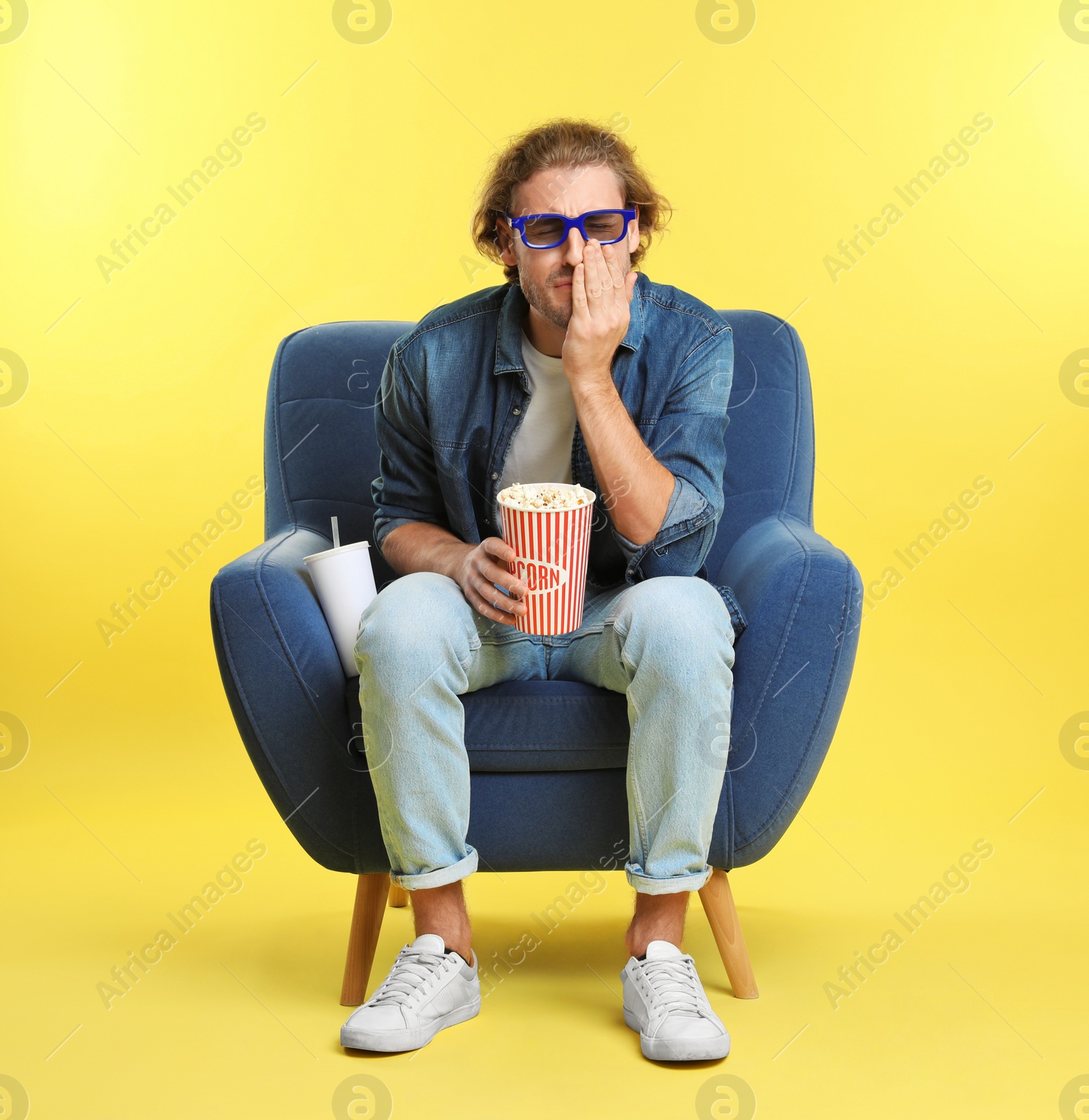 Photo of Emotional man with 3D glasses, popcorn and beverage sitting in armchair during cinema show on color background