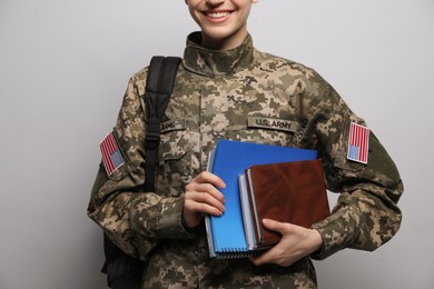 Female cadet with backpack and notebooks on light grey background, closeup. Military education