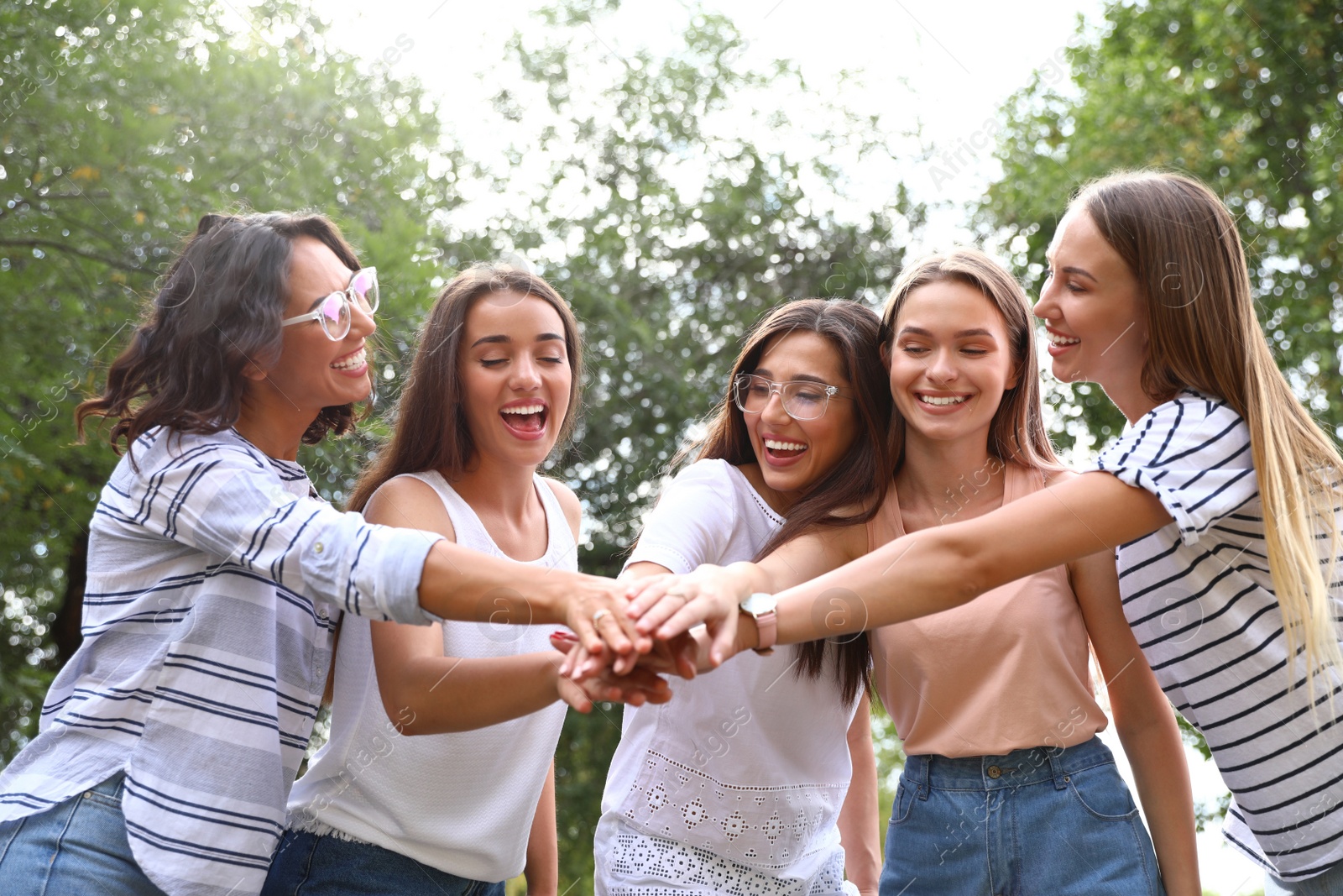 Photo of Happy women putting hands together outdoors on sunny day. Girl power concept