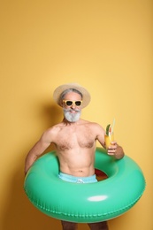 Shirtless man with inflatable ring and glass of cocktail on color background