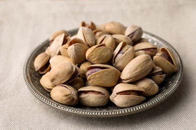 Photo of Plate with pistachio nuts on beige tablecloth, closeup