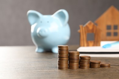 Photo of House models, stacked coins, piggy bank and notebook on wooden table, selective focus