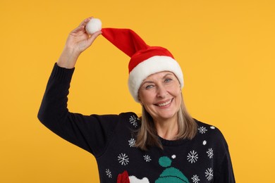 Happy senior woman in Christmas sweater and Santa hat on orange background