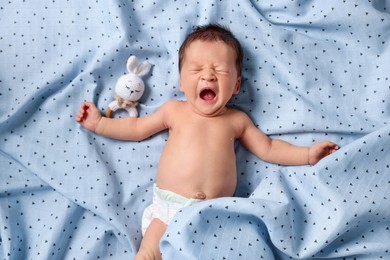 Cute newborn baby with toy bunny yawning on bed, top view
