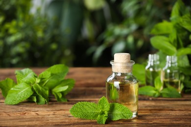 Photo of Bottle of mint essential oil and green leaves on wooden table, space for text