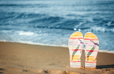 Photo of Stylish flip flops on sand near sea, space for text. Beach accessories