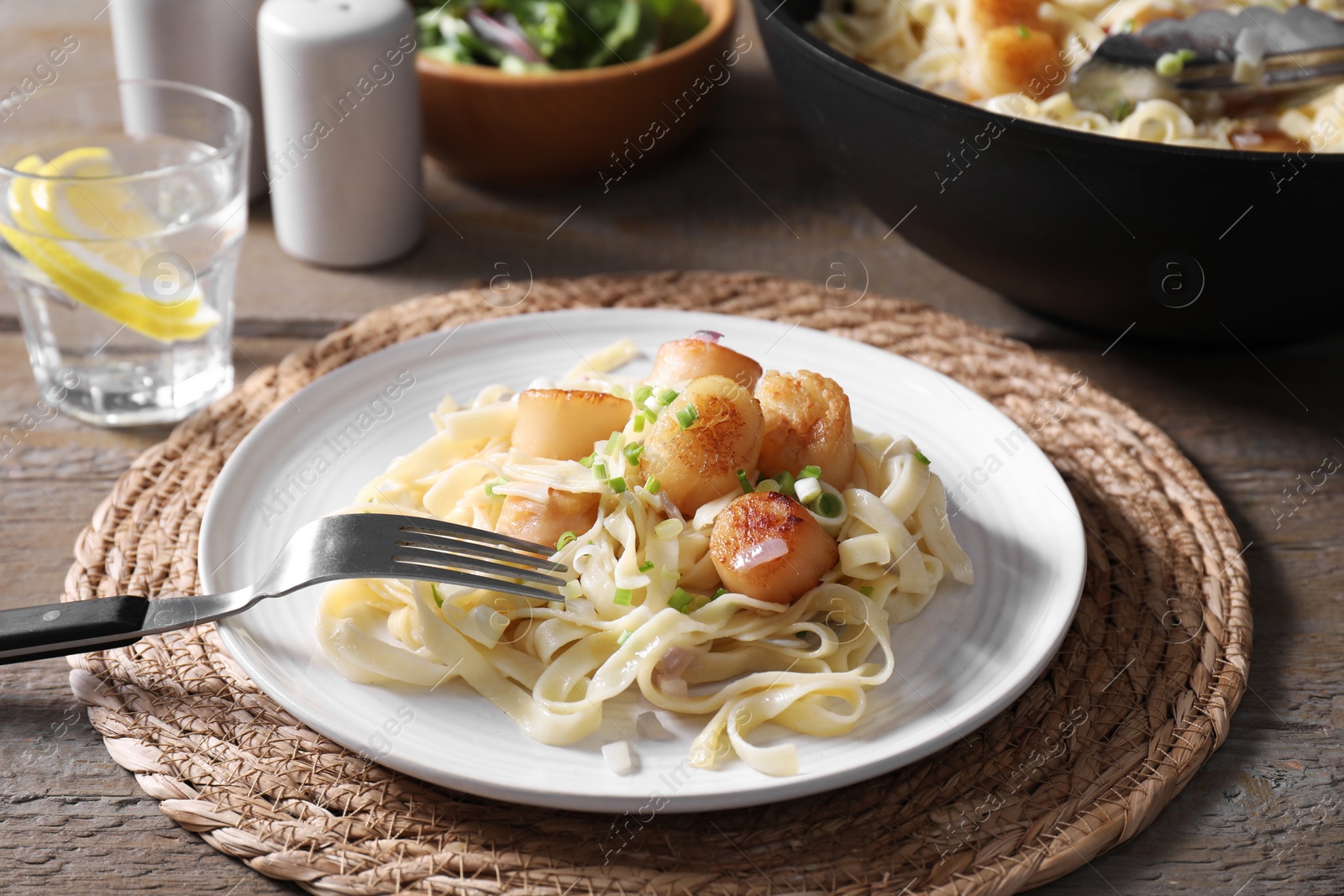 Photo of Delicious scallop pasta with onion served on wooden table, closeup