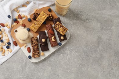 Different energy bars, nuts, blueberries, protein cocktail and powder on grey table, flat lay. Space for text