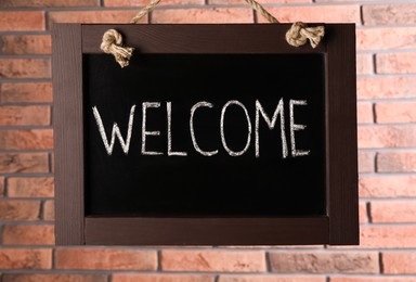 Photo of Small chalkboard with word Welcome hanging near brick wall