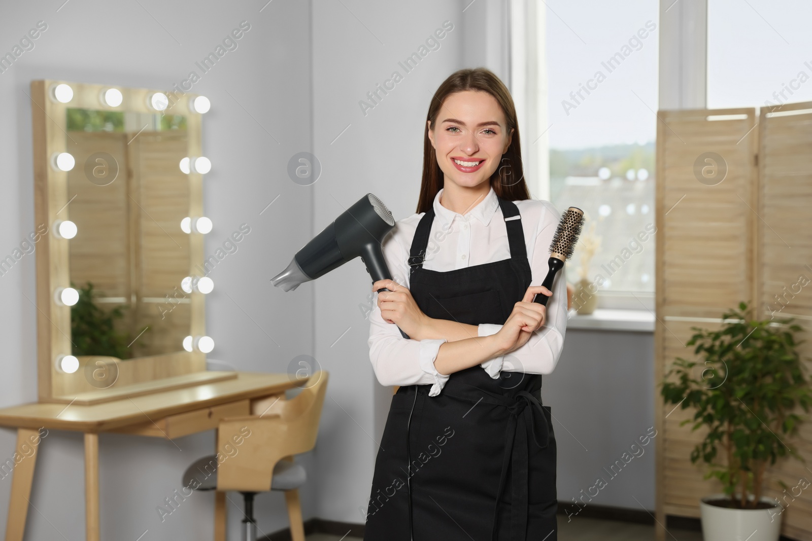 Photo of Portrait of happy hairdresser with hairdryer and brush in beauty salon