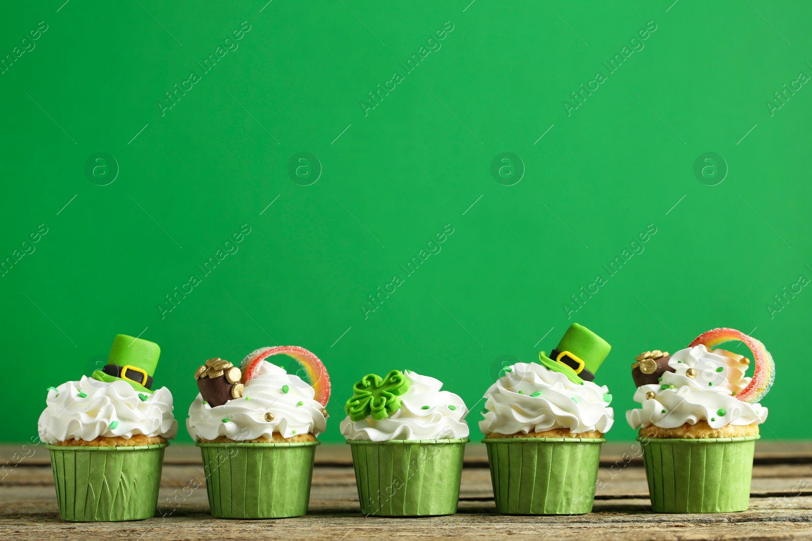Photo of St. Patrick's day party. Tasty festively decorated cupcakes on wooden table. Space for text