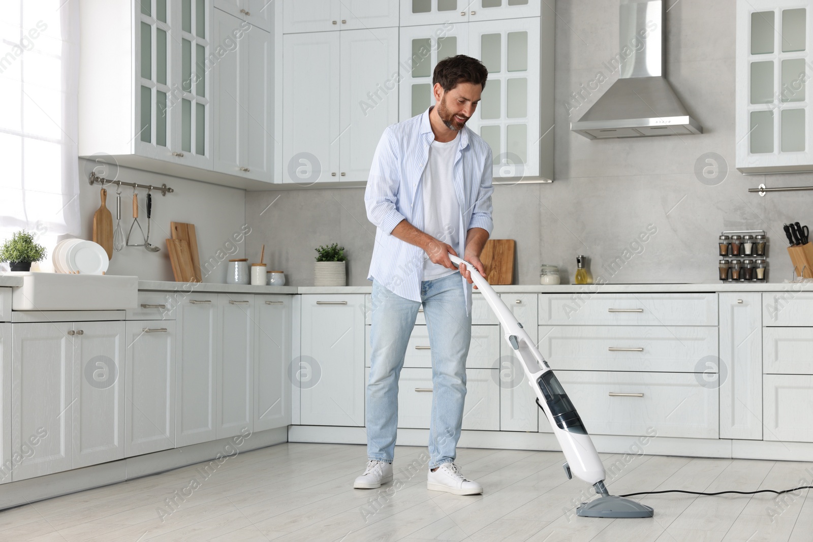 Photo of Happy man cleaning floor with steam mop in kitchen at home