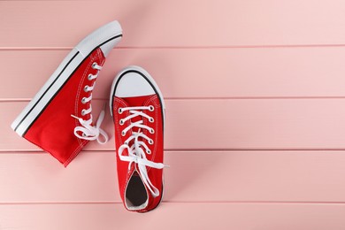 Pair of red sneakers on pink wooden table, flat lay. Space for text