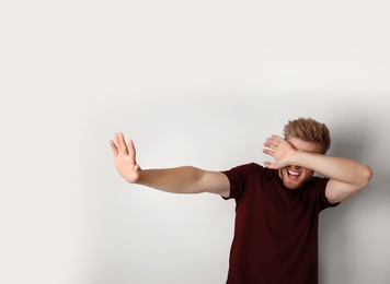 Photo of Young man being blinded and covering eyes with hand on light background
