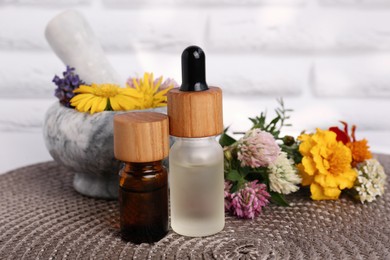 Glass bottles of essential oil, mortar with pestle and different wildflowers on wicker mat