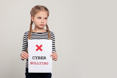 Photo of Girl holding sign with phrase Cyber Bullying on light grey background, space for text