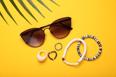 Stylish sunglasses, bracelets and rings on yellow background, flat lay