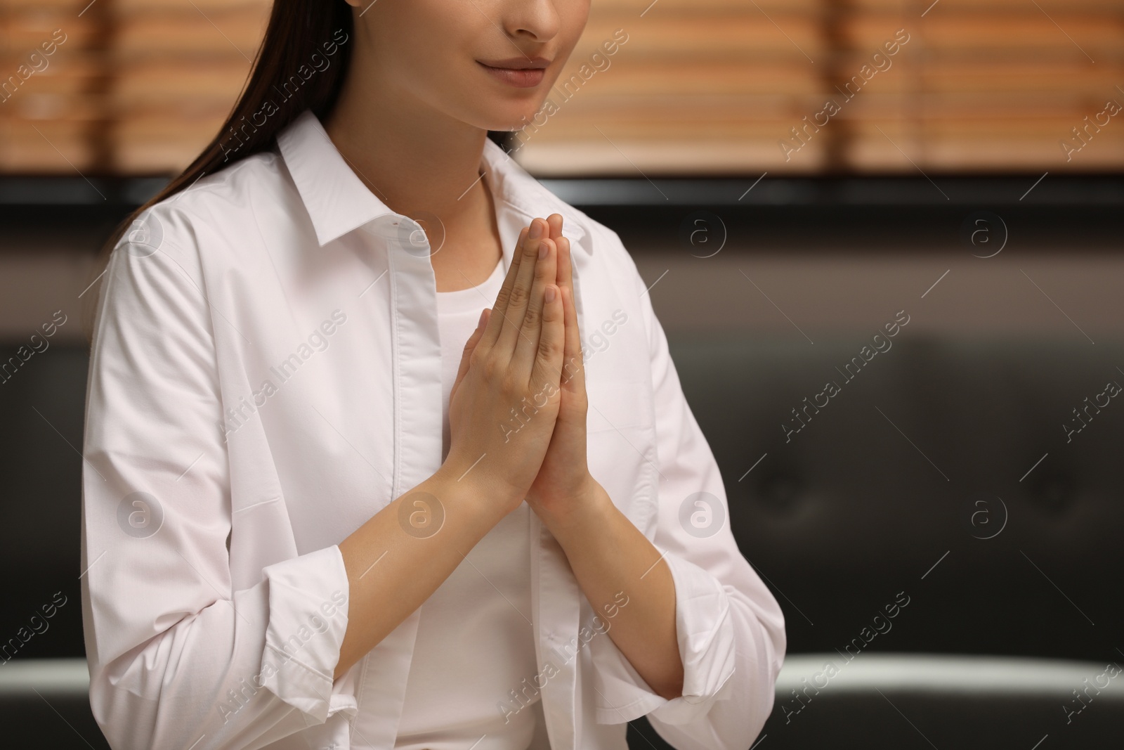 Photo of Religious woman with clasped hands praying indoors, closeup