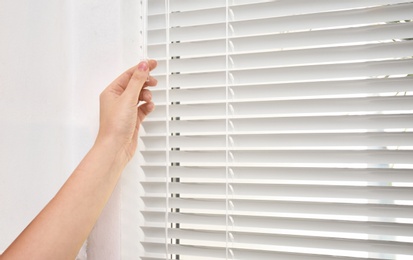 Photo of Woman opening white horizontal window blinds, closeup
