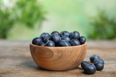 Photo of Bowl of fresh blueberries on wooden table against blurred green background