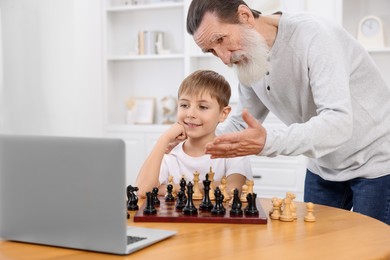 Photo of Grandfather teaching his grandson to play chess following online lesson at home