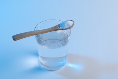 Photo of Glass of water and spoon with baking soda on light blue background. Space for text