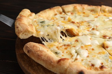 Taking piece of delicious cheese pizza at wooden table, closeup