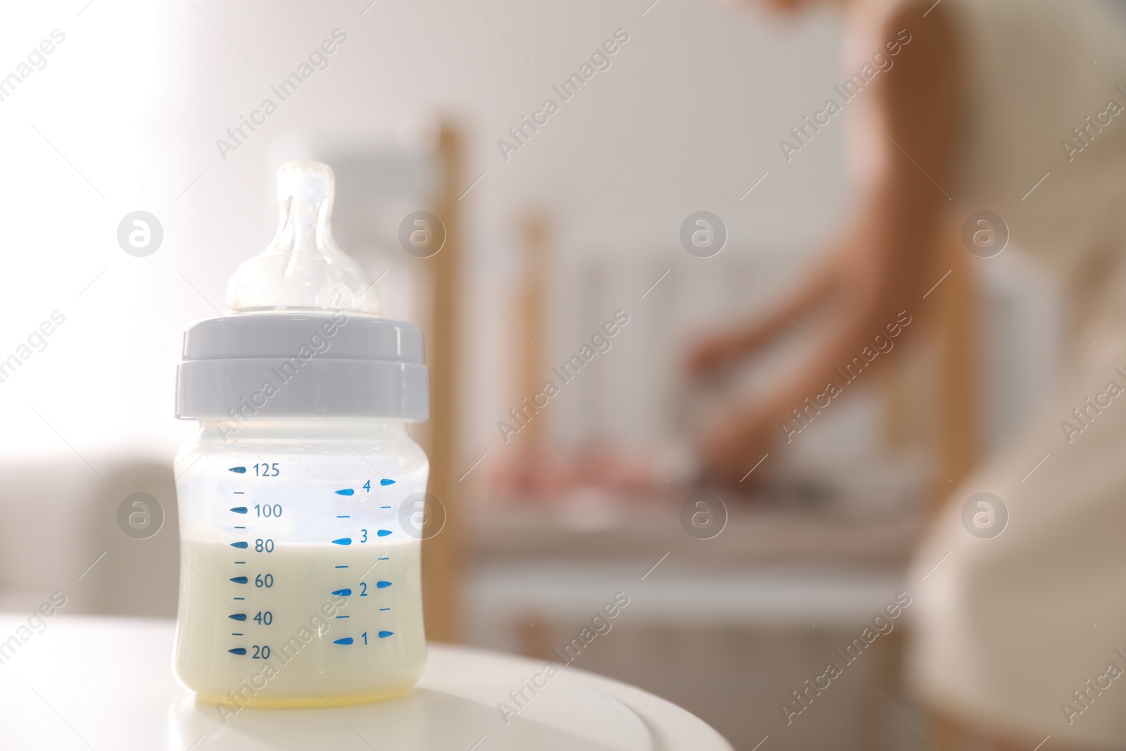 Photo of Mother and little baby indoors, focus on table with bottle of milk