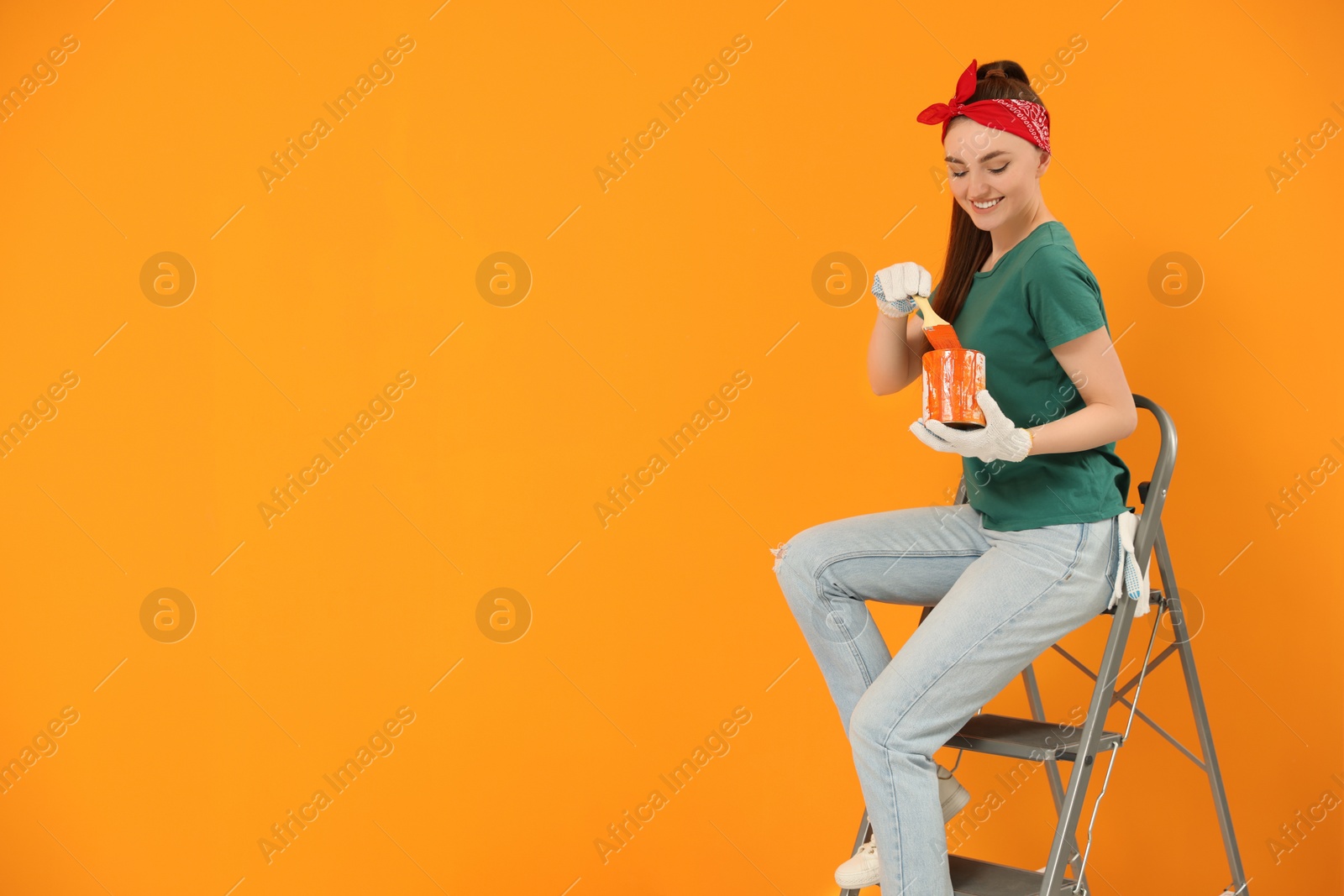 Photo of Happy designer with brush taking paint from can near orange wall, space for text