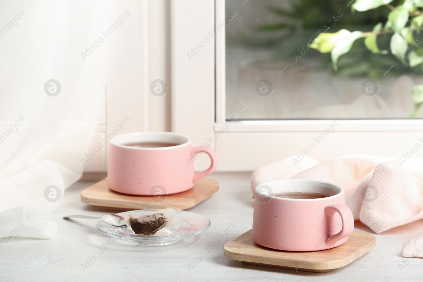 Photo of Cups of hot tea with wooden coasters on window sill