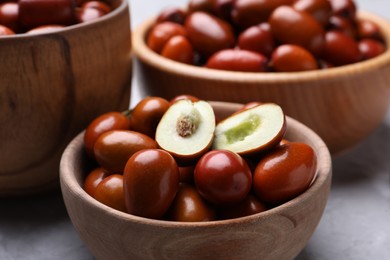 Photo of Fresh Ziziphus jujuba fruits in wooden bowls on table, closeup