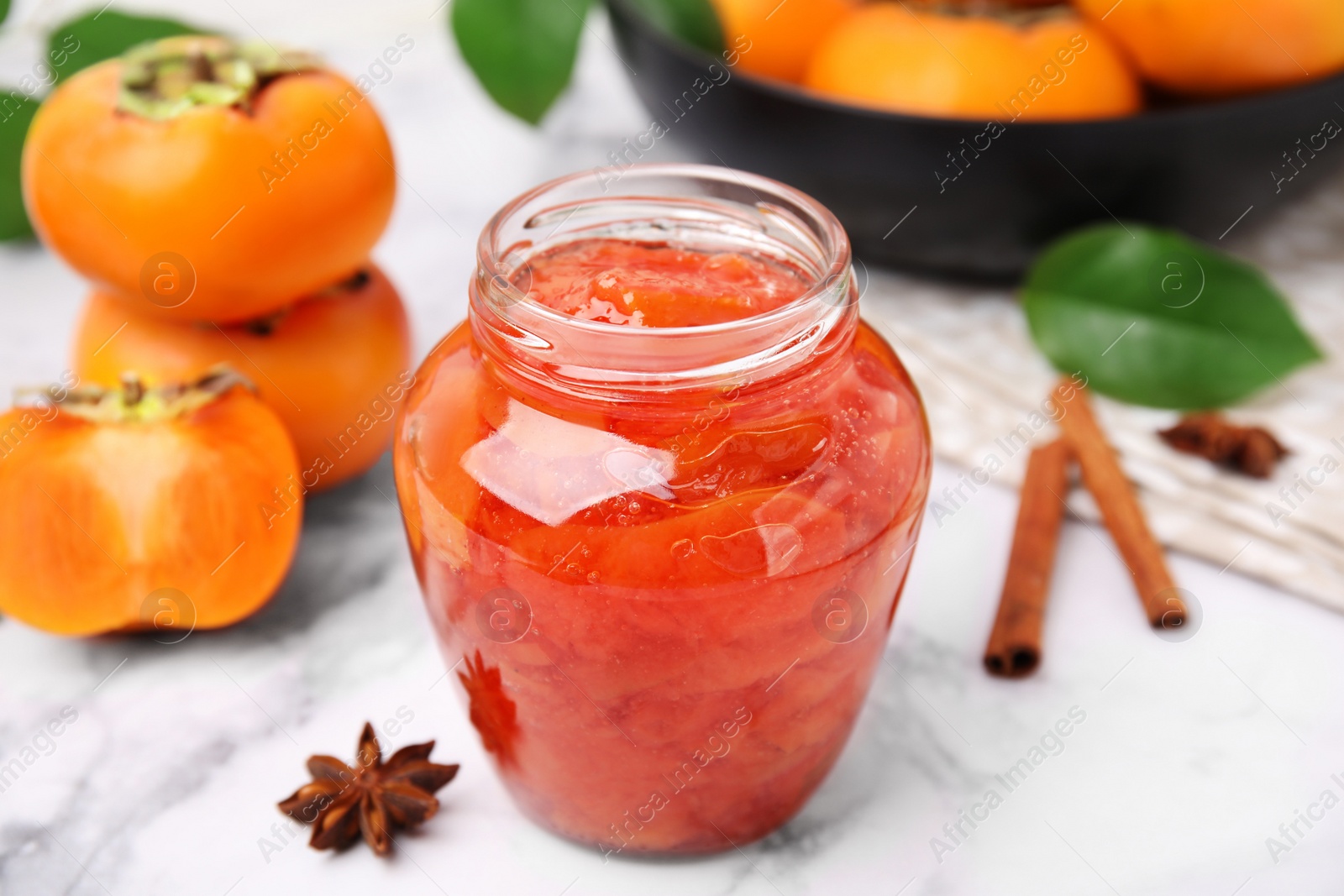 Photo of Jar of tasty persimmon jam and ingredients on white marble table