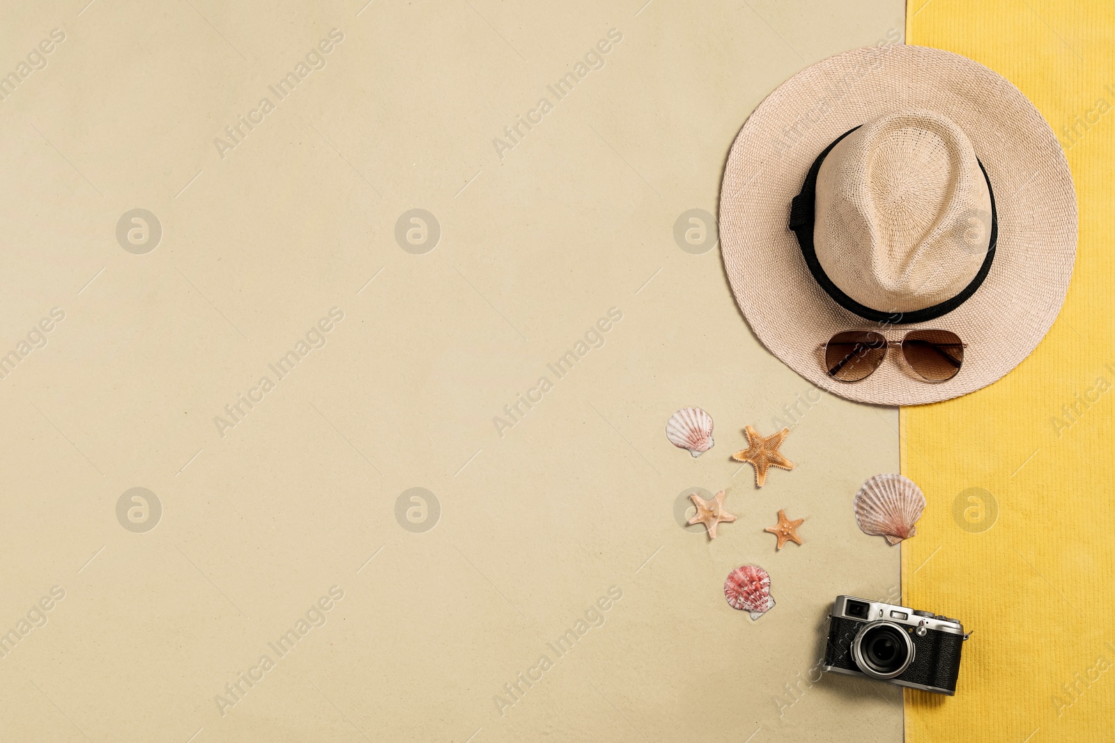 Photo of Beach towel, hat, sunglasses, camera, starfishes and sea shells on sand, flat lay. Space for text