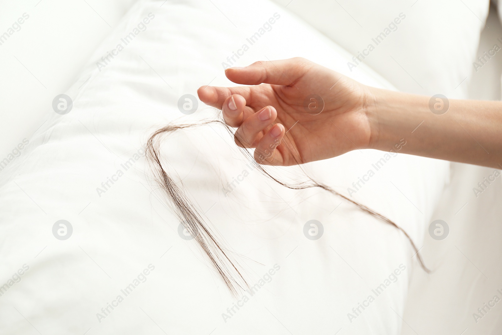 Photo of Woman picking fallen long hair from pillow, closeup