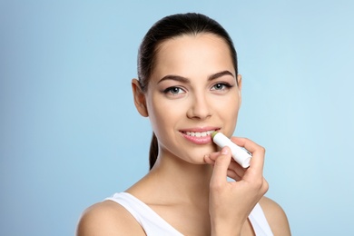 Young woman applying balm on her lips against color background