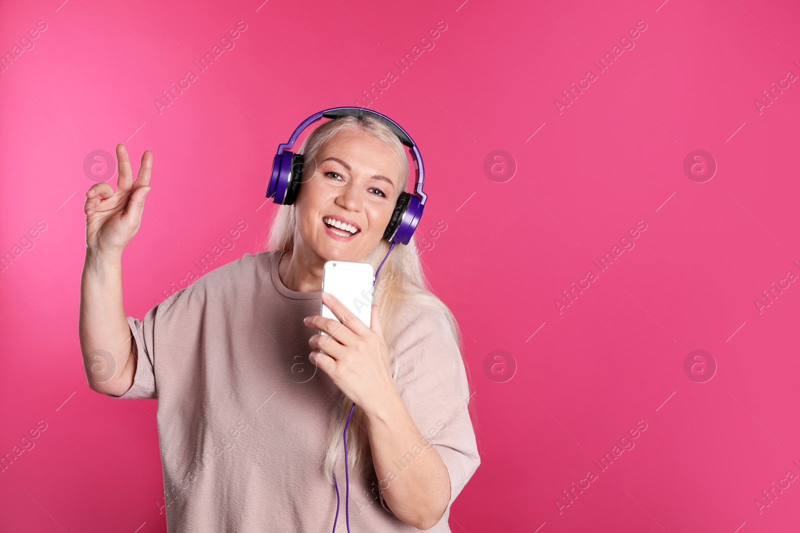 Photo of Mature woman in headphones with mobile device on color background. Space for text