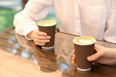 Women holding takeaway paper cups at table, closeup. Coffee to go