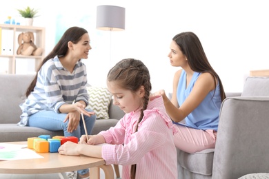 Little girl drawing at table while child psychologist talking with her mother in office