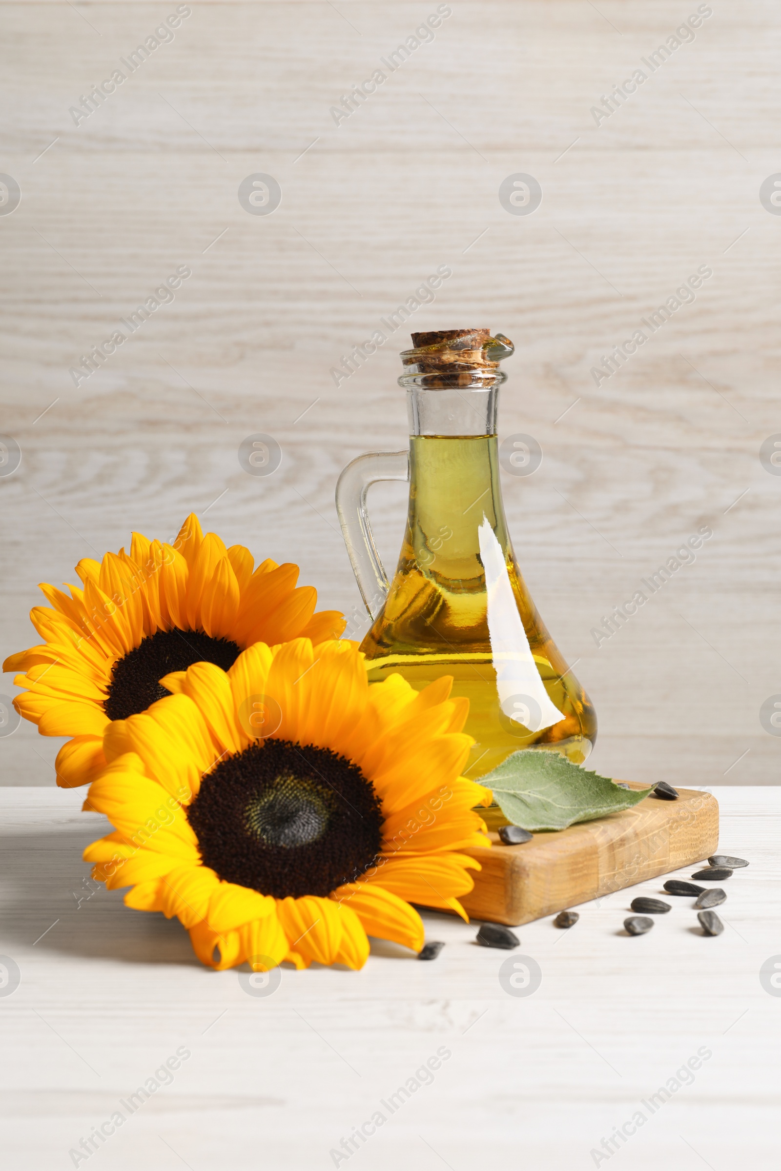 Photo of Sunflower cooking oil, seeds and yellow flowers on white wooden table