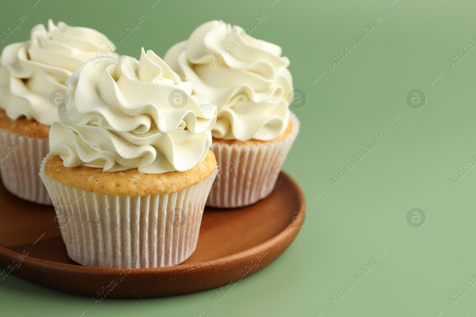 Photo of Tasty vanilla cupcakes with cream on green background, closeup. Space for text