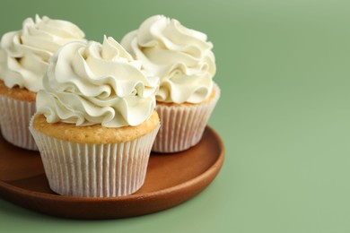 Tasty vanilla cupcakes with cream on green background, closeup. Space for text