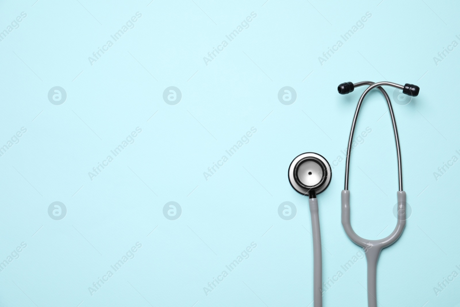 Photo of Stethoscope on light blue background, top view. Space for text