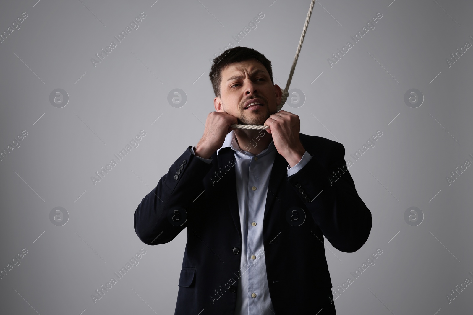 Photo of Depressed businessman with rope noose on neck against light grey background