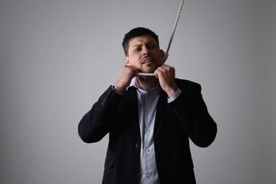 Depressed businessman with rope noose on neck against light grey background