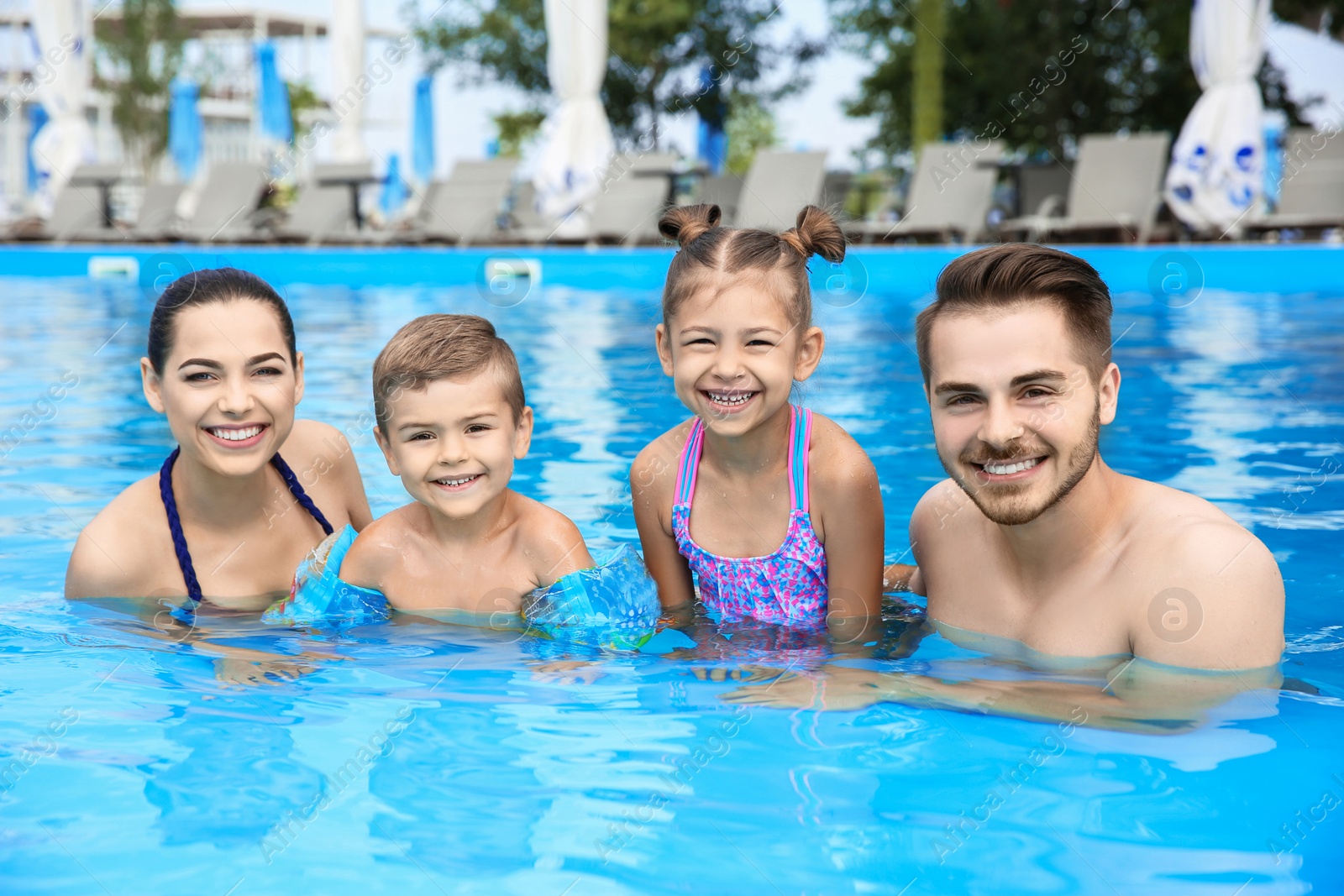 Photo of Young family with little children in swimming pool on sunny day