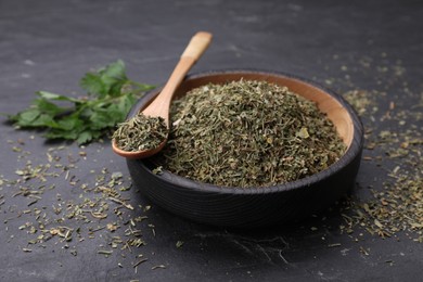 Photo of Plate and spoon with dried parsley on black table, closeup