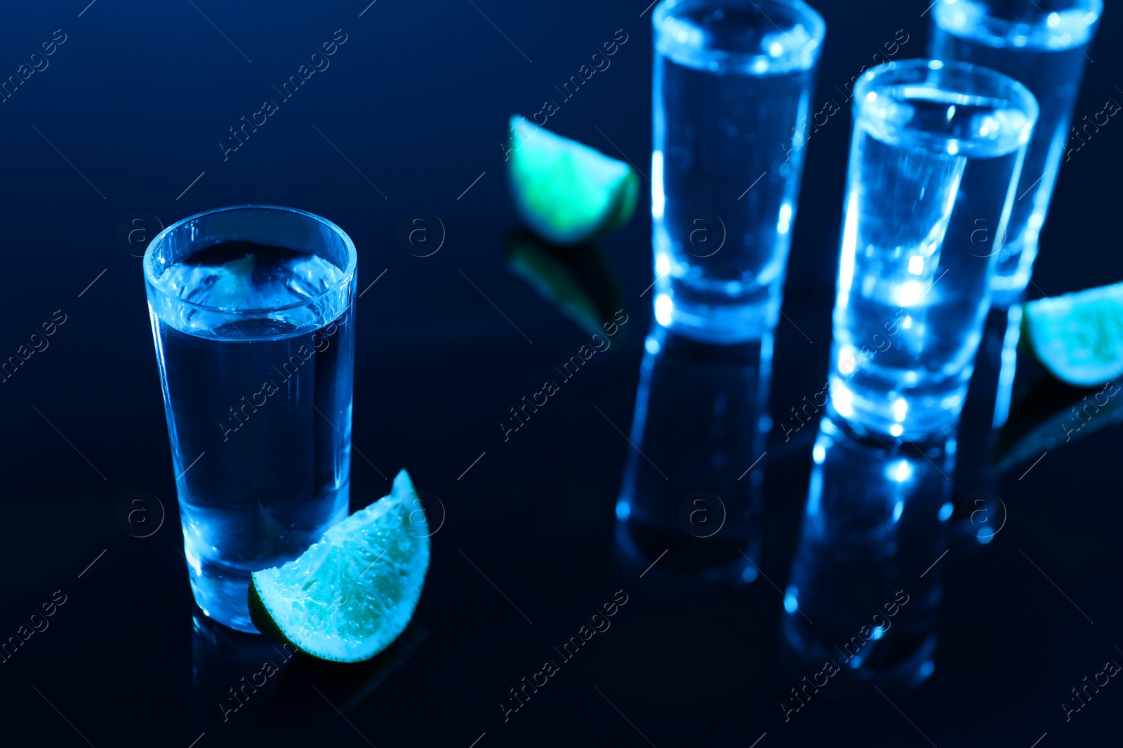 Photo of Shot glasses of vodka with lime slices on dark background