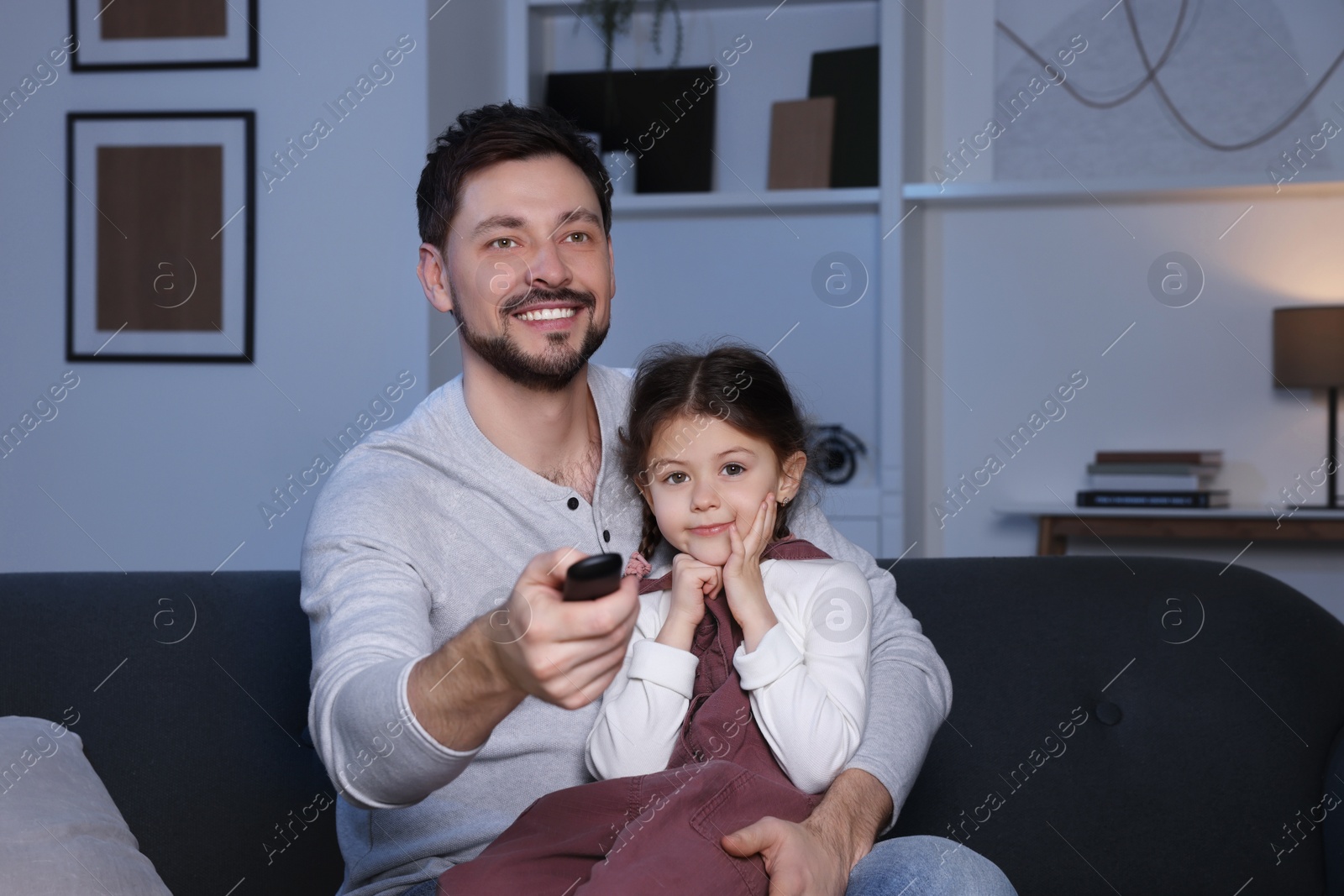 Photo of Father and daughter at home. Happy man changing TV channels with remote control