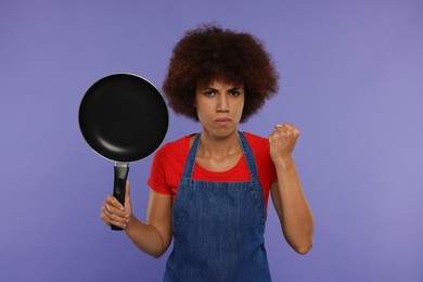 Photo of Angry young woman in apron holding frying pan on purple background